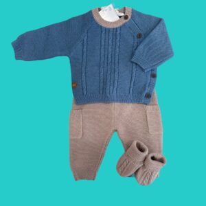 Blue cable-knit baby sweater with a beige collar and matching beige pants laid against a teal background