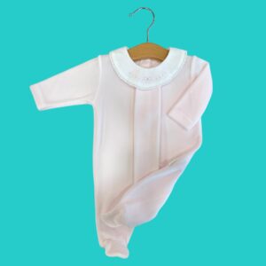 White baby onesie with a lace-trimmed Peter Pan collar hanging on a wooden hanger against a teal background.