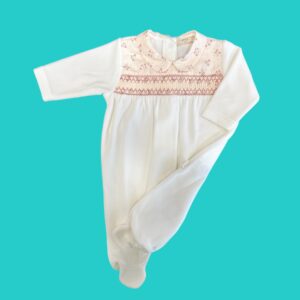 White baby onesie with a pink floral smocked yoke and Peter Pan collar on a teal background