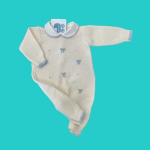 Cream-colored knitted baby sweater with blue bow embellishments, floating on a teal background, tag visible near the collar.